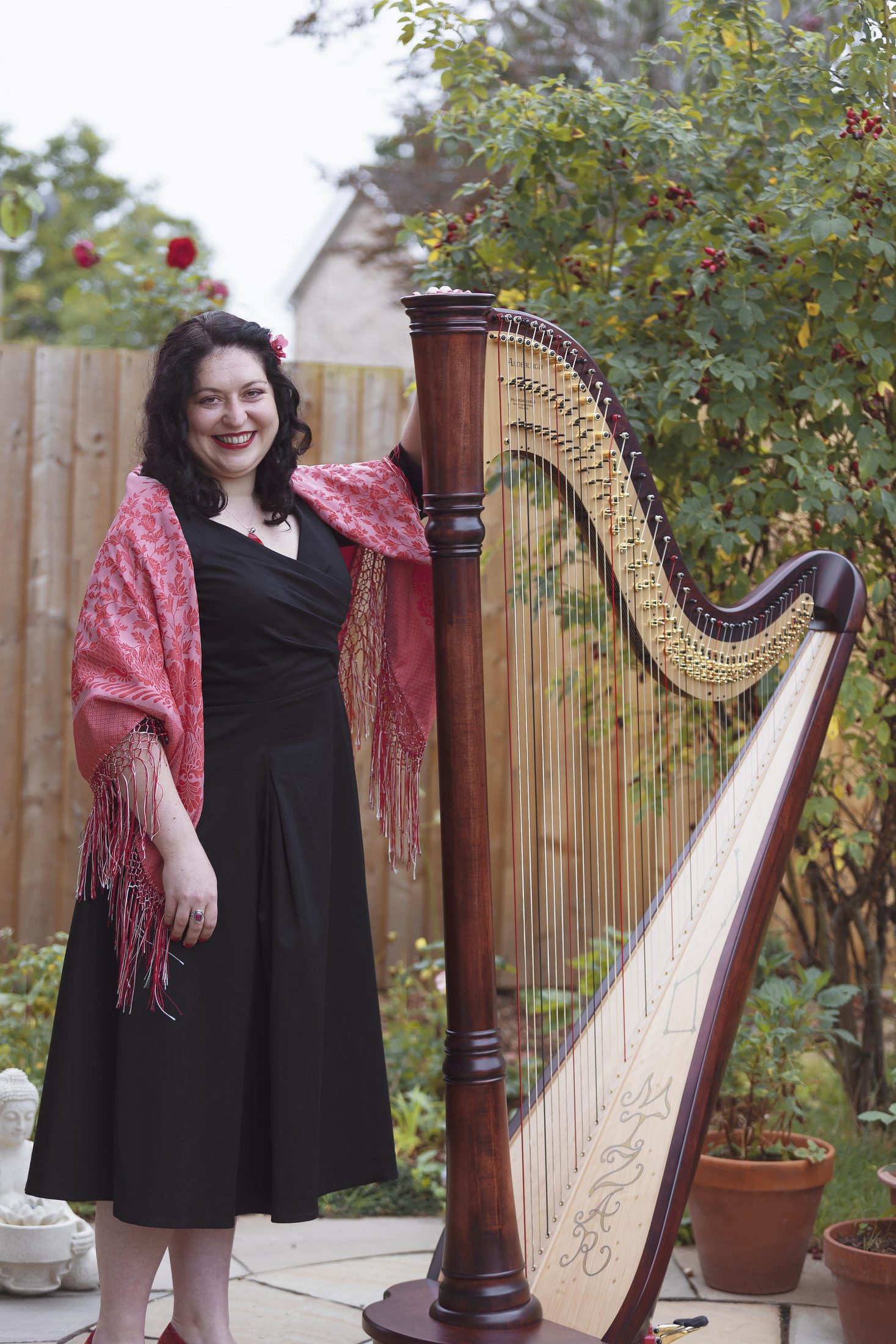 Maria standing beside her harp in a garden