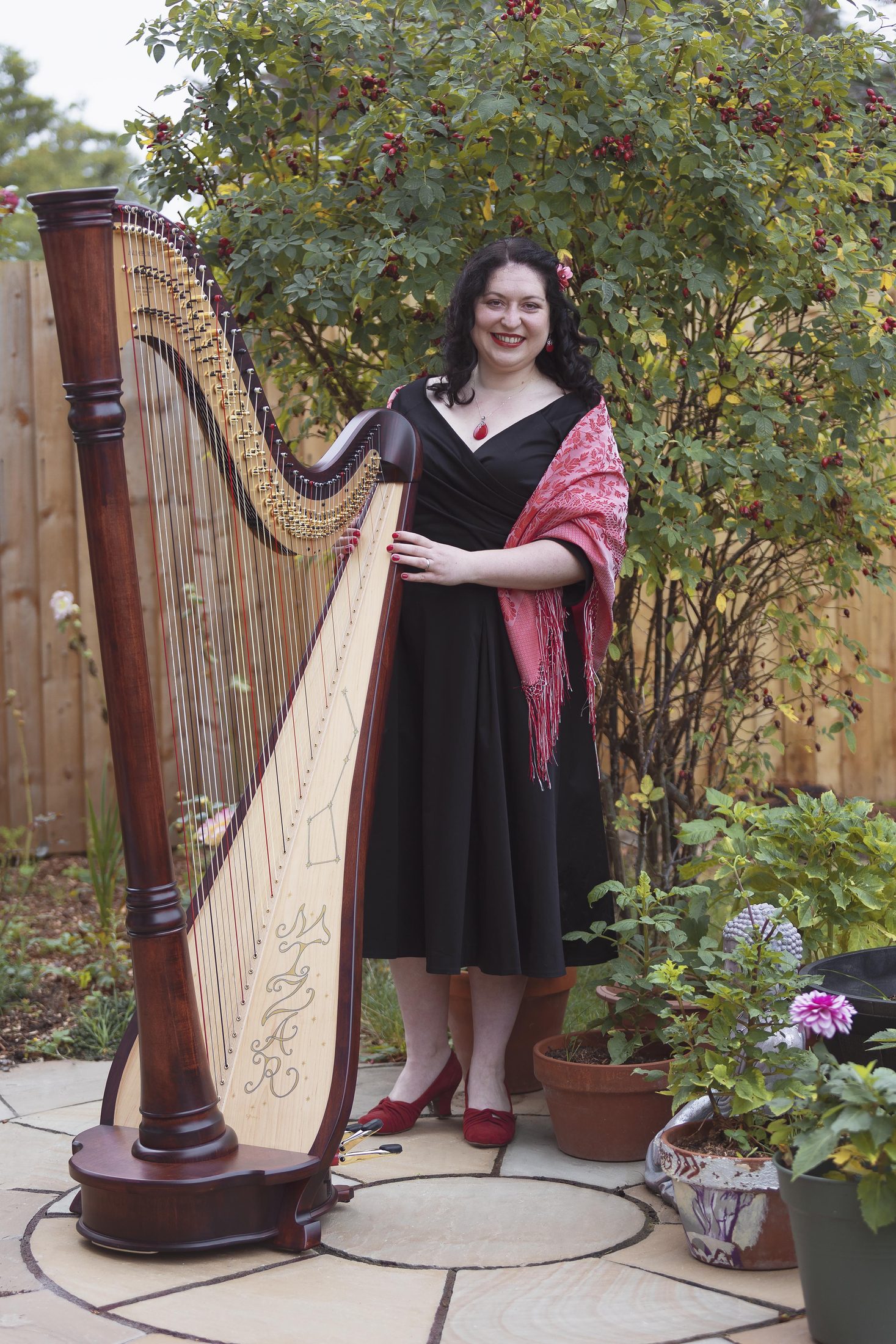 Maria Trotter standing with her harp in a garden