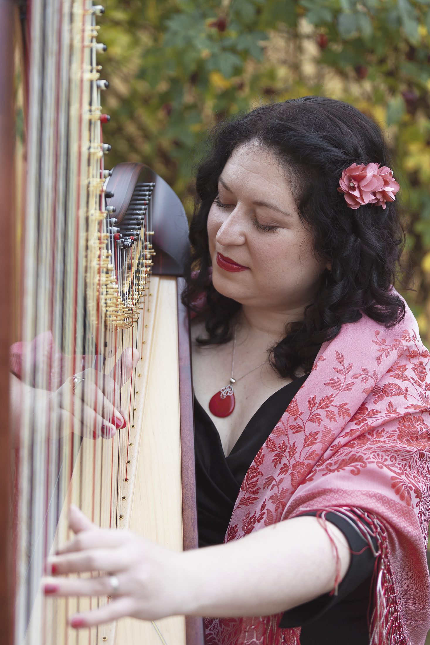 Maria playing harp outdoors with focused attention