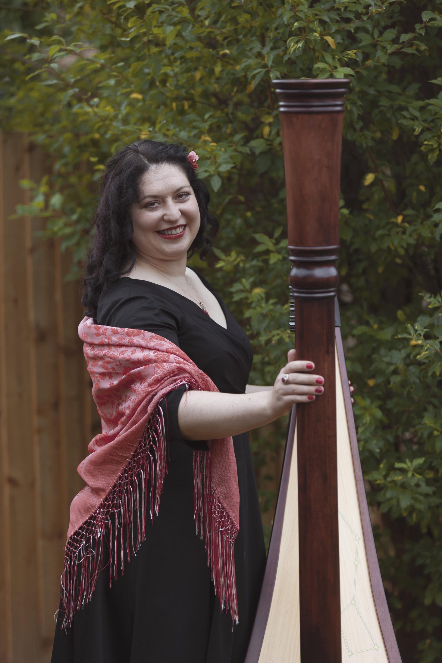 Maria standing beside her harp in a garden
