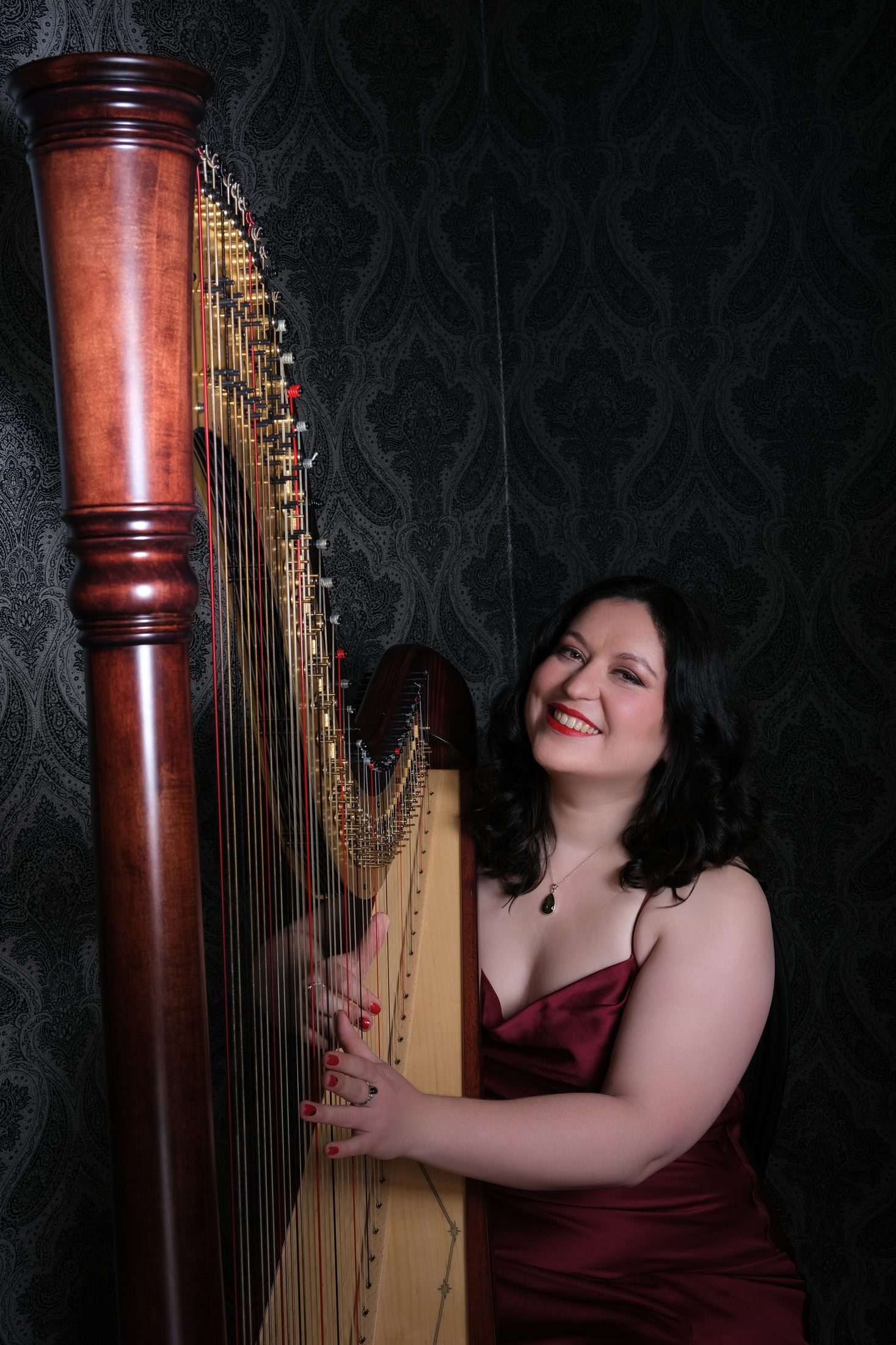 Maria smiling beside her harp in a studio portrait